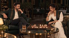 Scene 52 Dario sits in the left armchair and Sepsut in the right, relaxing over backgammon and drinks after closing, with the dining room lights off.